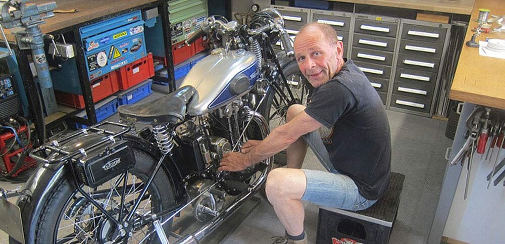 Kollege sitzt auf einer Kiste vor seinem Motorrad in seiner Werkstatt