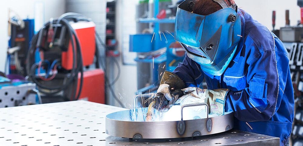 Azubi an Schweißtisch mit Schweißhelm