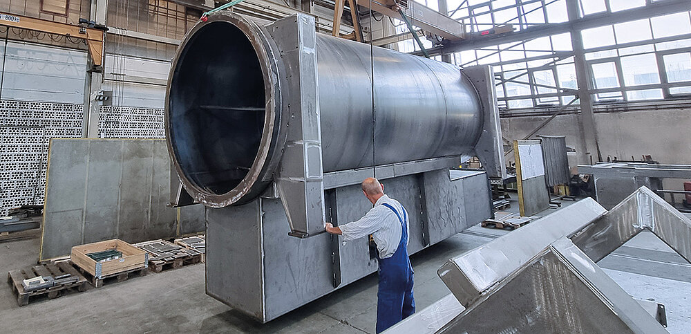 Mitarbeiter bedient Kran mit sehr großem Bauteil