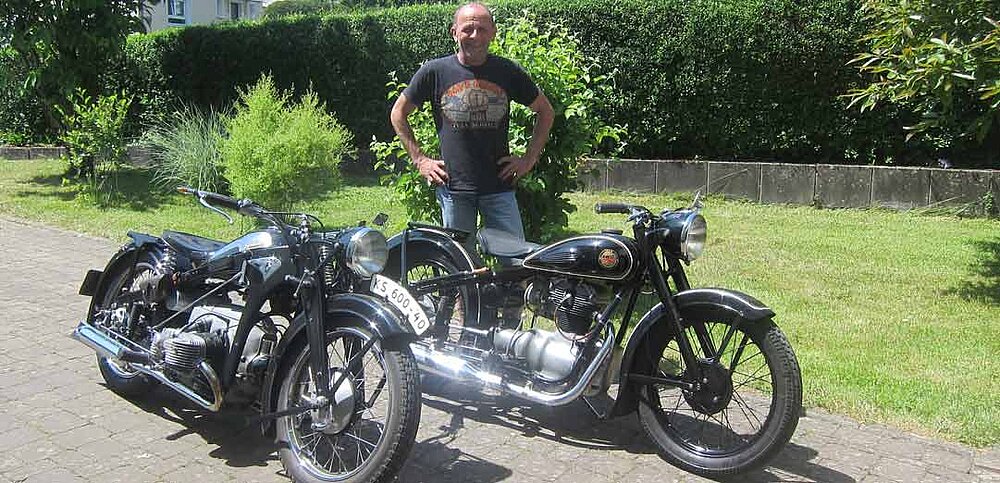 Kollege präsentiert in einer Einfahrt zwei seiner historischen Motorräder