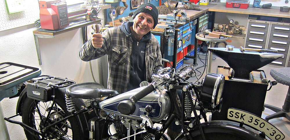 Kollege sitzt in seiner Werkstatt und zeigt den Daumen nach oben