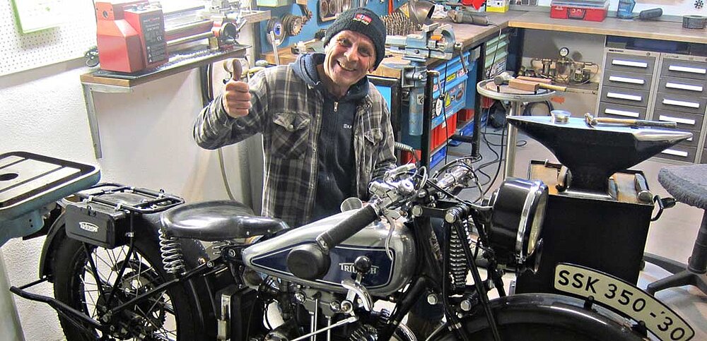 Kollege sitzt in seiner Werkstatt und zeigt den Daumen nach oben