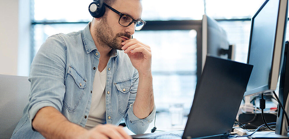 IT-Mitarbeiter mit Headset an Laptop und PC