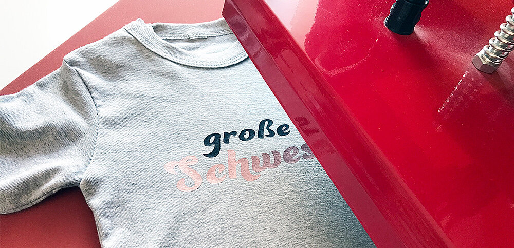 Ein graues T-Shirt wird mit dem Schriftzug "Große Schwester" bedruckt