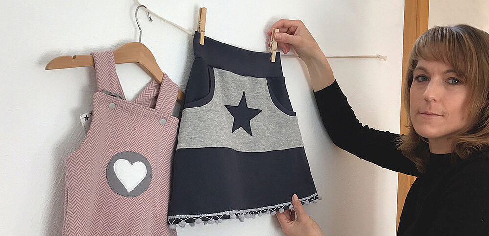 Kollegin hängt zwei fertige Kleidungsstücke an Leine auf